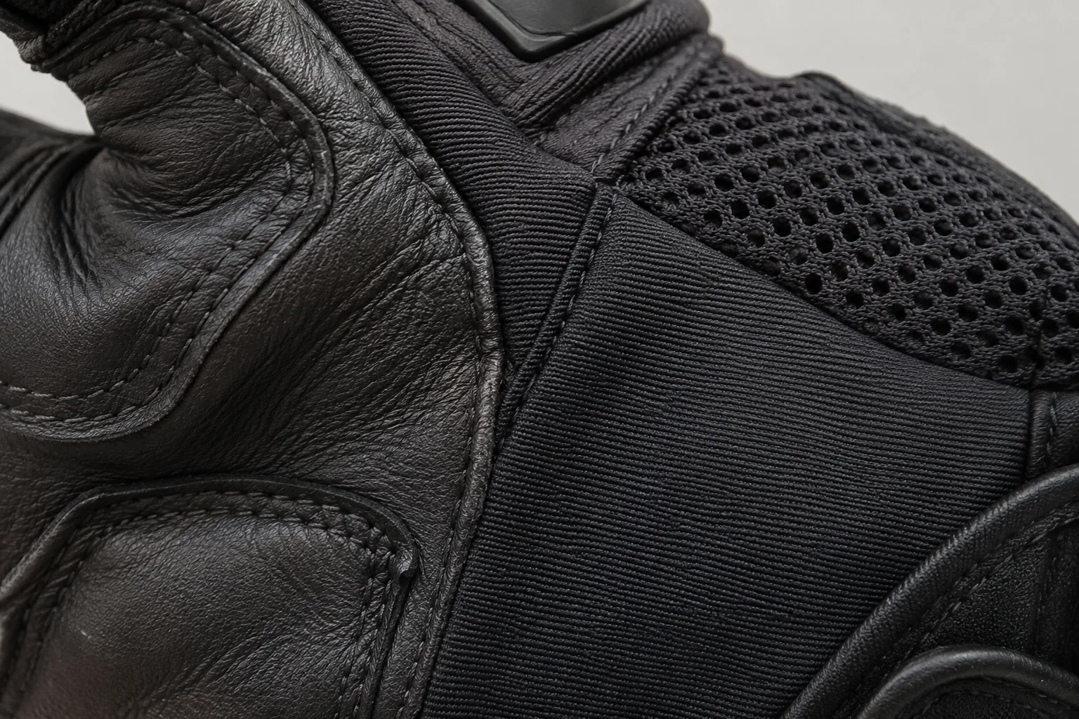 Gros plan sur les coutures reliant le cuir, le textile et le mesh d’un gant de moto.