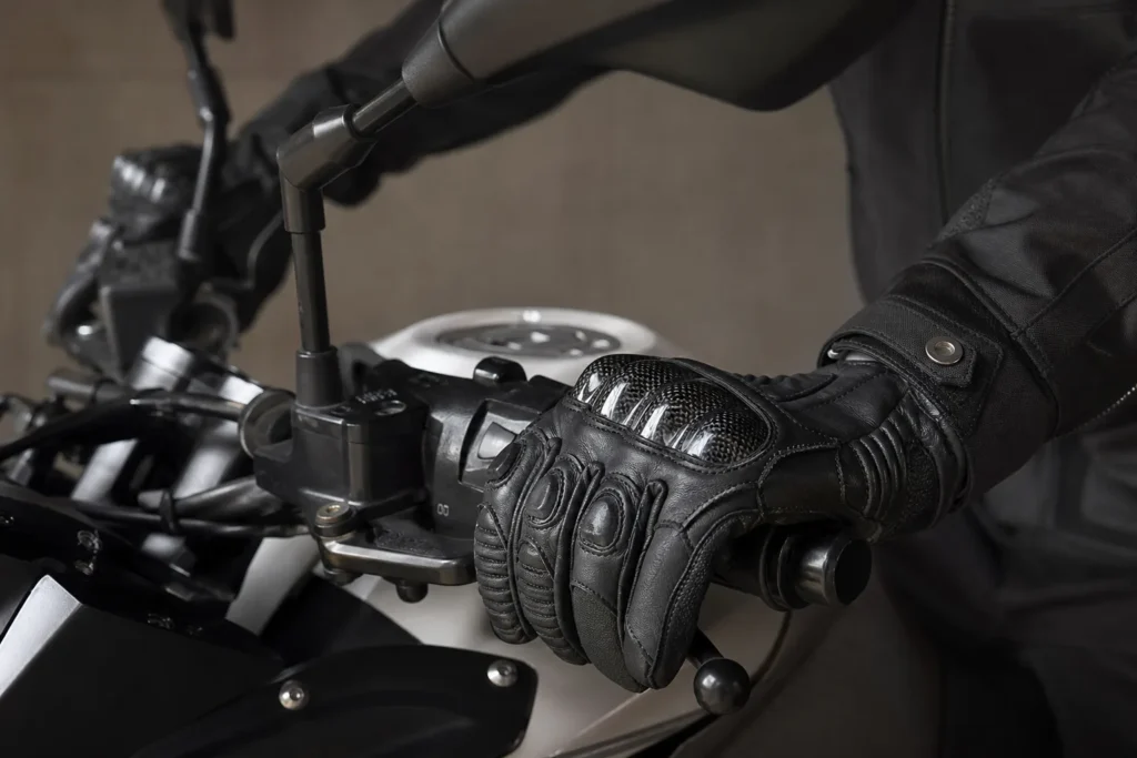 Mains gantées posées sur les commandes d’un guidon de moto à l’arrêt.